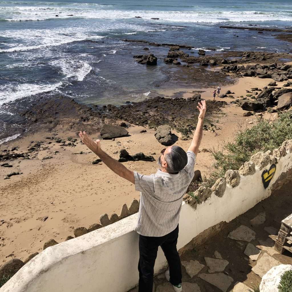 In this stunning photo, we see Michael gazing out at the vast, blue ocean at Bafureira beach in Portugal. His attention drawn to the horizon where the deep blue sea meets the clear blue sky. The waves gently crash against the shore, the sound of their rhythmic crashing a soothing soundtrack to the peaceful scene. The golden sands of Bafureira beach stretch out as far as the eye can see, inviting us to come and soak up the sun and the stunning surroundings. It's easy to see why Bafureira beach is such a popular destination for travelers and locals alike, with its crystal-clear waters, golden sands, and breathtaking views. So, this photo perfectly captures the beauty and serenity of this amazing place.