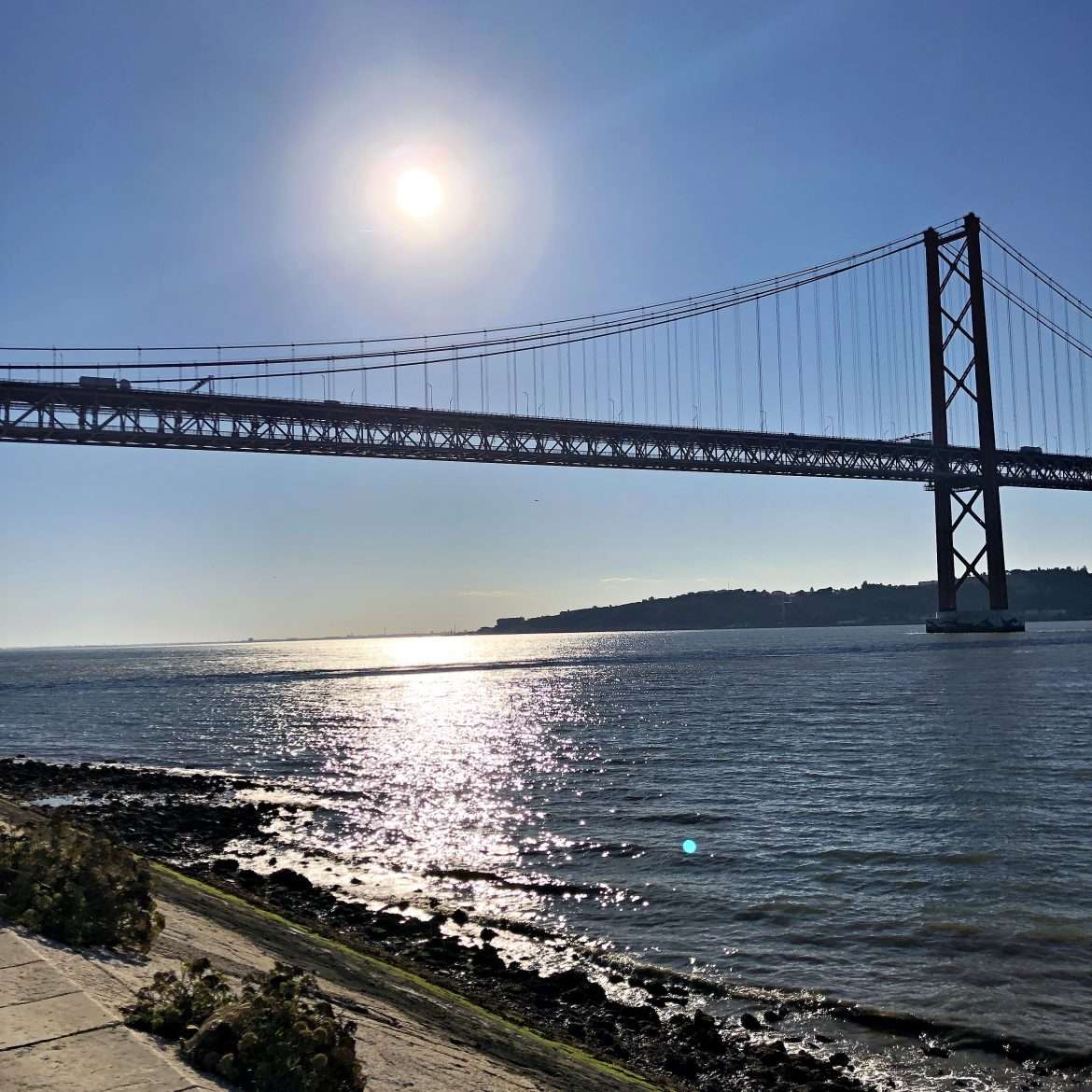 Picturesque view of the April 25th Bridge in Lisbon, Portugal, with sunlight reflecting on the water.