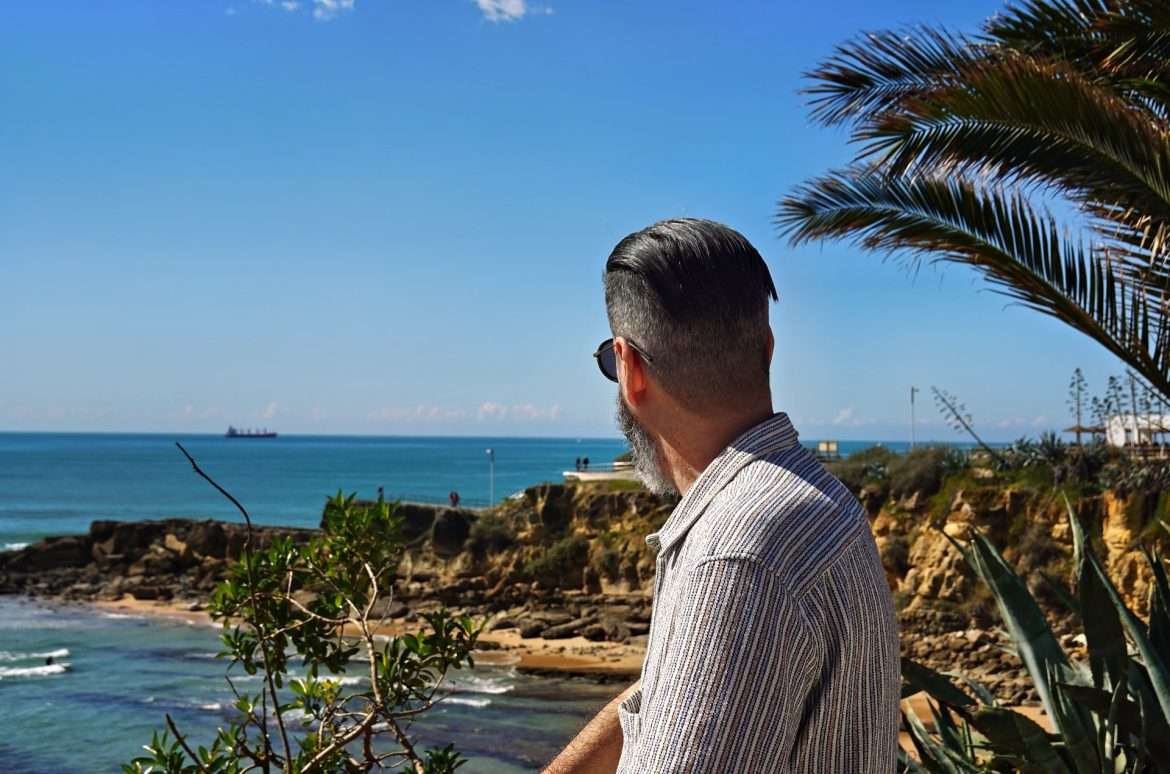 A man stands by the ocean, deep in thought, reflecting on the road less traveled.