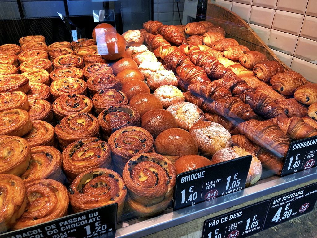 A bakery display filled with golden croissants and Pão de Deus pastries.