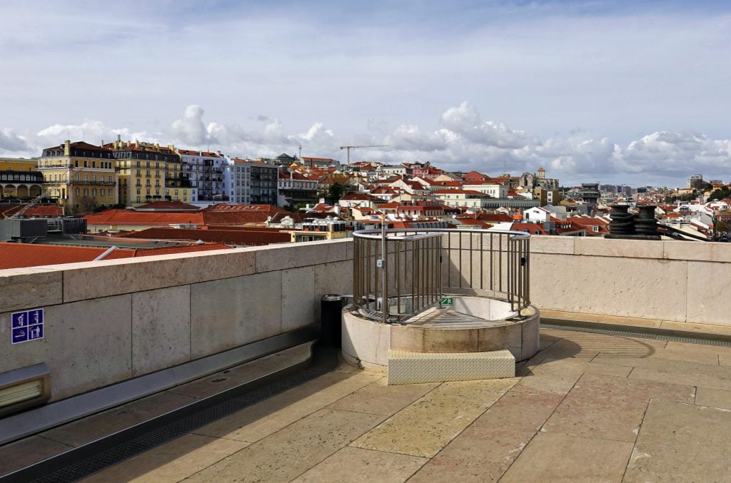 Elevated viewing deck providing a panoramic view of the colorful buildings of Lisbon, with safety railings and accessibility signs.