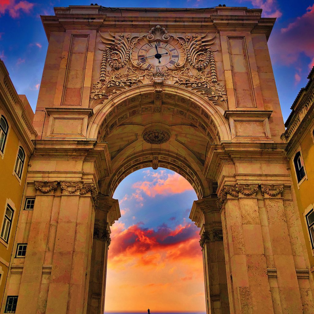 The grand Rua Augusta Arch, bathed in the golden hues of the setting sun, set against a backdrop of a vibrant sky.