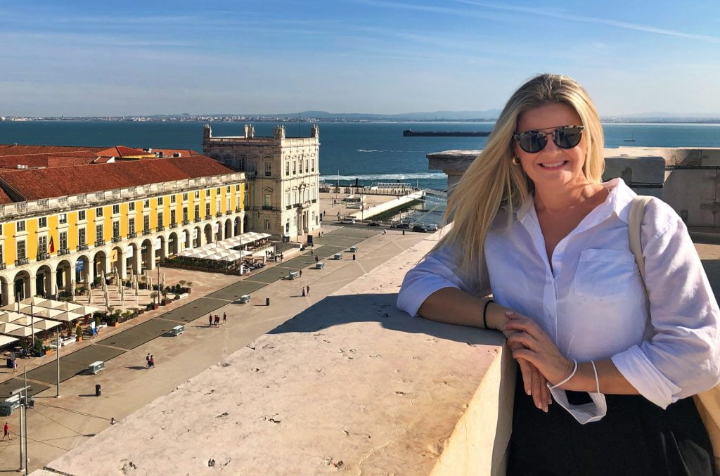 Smiling woman in sunglasses enjoying a panoramic view of Lisbon with Rua Augusta Arch visible below.