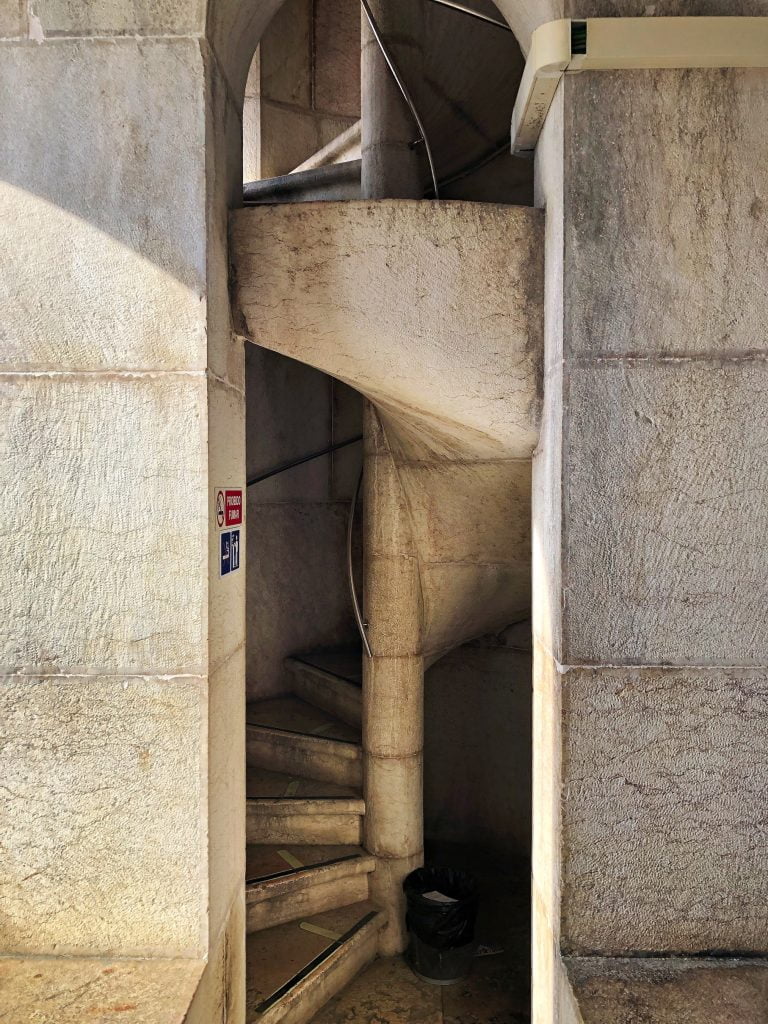 A tight spiral staircase tucked away between stone walls in Lisbon at Rua Augusta Arch.