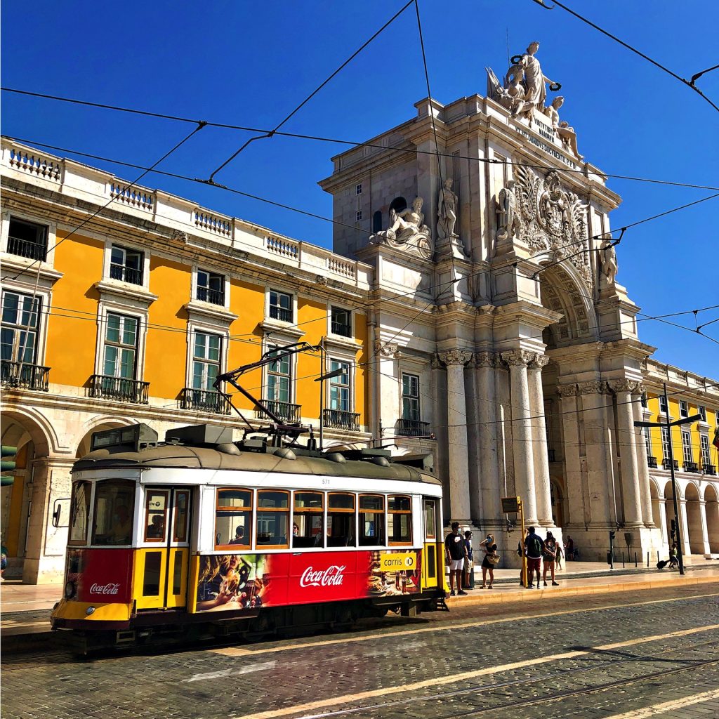 A colorful tram adorned with advertisements passing by the ornate Rua Augusta Arch in Lisbon, Portugal.