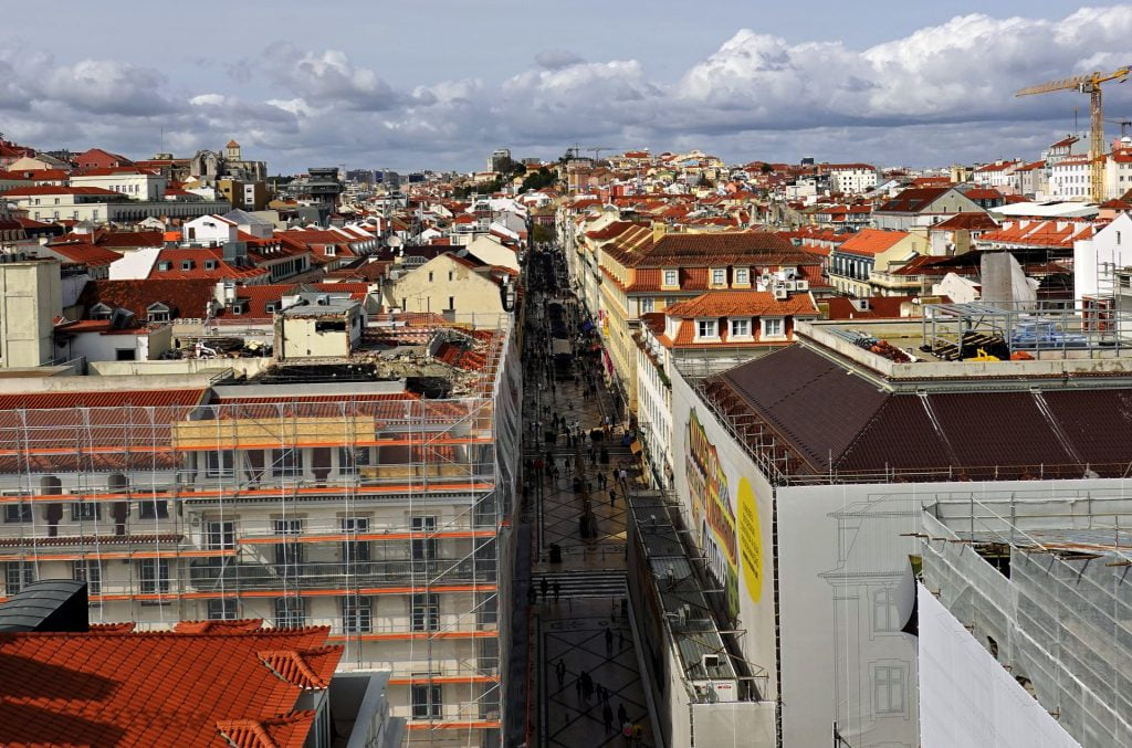 Overhead view of a bustling street in Lisbon, showcasing red rooftops, pedestrians, and advertisements.