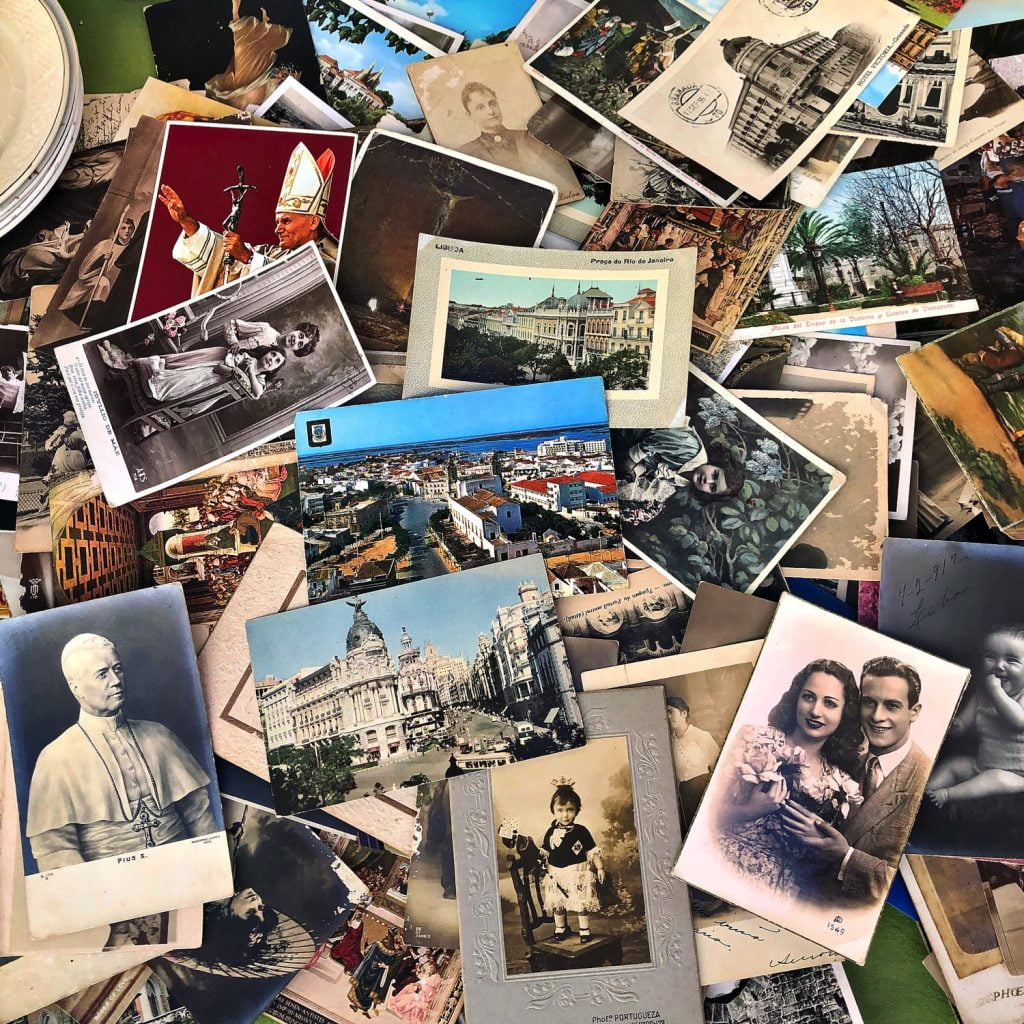 An assortment of vintage postcards and photographs spread out on a table, featuring various historical figures, landmarks, and personal portraits.