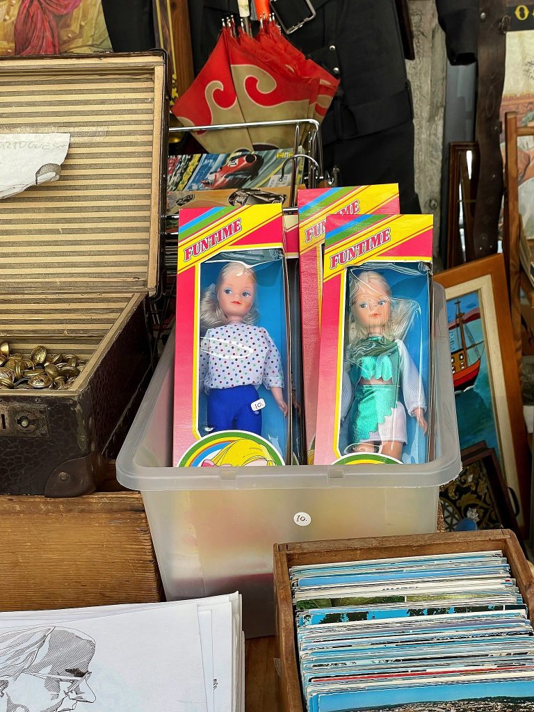 Vintage dolls in original packaging displayed among assorted items at a flea market stall.